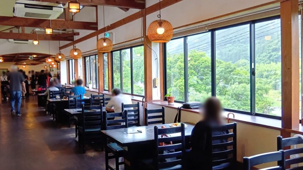 大きな窓から渓谷を眺めながら食事をしている人々。外の光がやんわりと差し込み、山の上のログハウス的な雰囲気。素晴らしい眺めです。