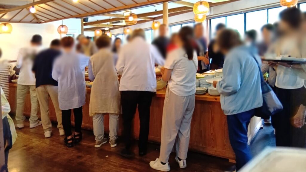 バイキングスタートした瞬間に、料理に集まる人々。あまりに人が多く、遠くから眺めている"筆者はる"。